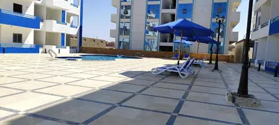 a pool with a blue umbrella and chairs and a table at اويسيس مارينا in Hurghada