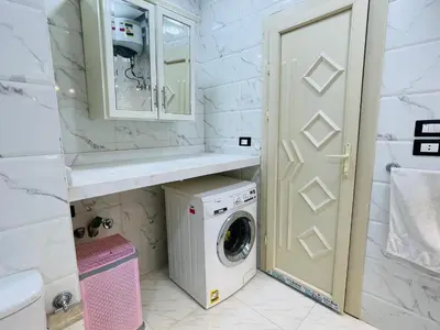 a white bathroom with a washing machine and a sink at Comfortable & Modern Appartement in Luxor