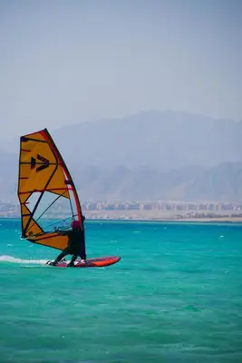 a person on a surfboard with a sail in the water at Sun Beach Hotel ABO SOMA in Hurghada