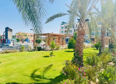 a park with palm trees and a building in the background at Hub resort Aqua park in Hurghada