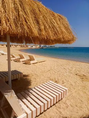 a group of lounge chairs and a straw umbrella on a beach at marvel princes in Hurghada