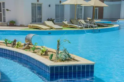 a large swimming pool with chairs and an umbrella at Cozy one bedroom apartment in AquaPalms resort in Hurghada