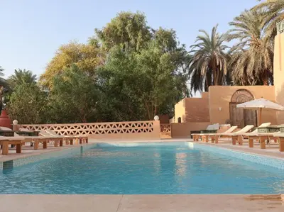 a swimming pool in a resort with benches and trees at Habu Hotel in Al Aqālitah