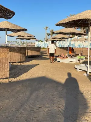 a shadow of a man walking on a beach with umbrellas at CHALET IN HURGHADA SCANDIC ReSORT in Hurghada