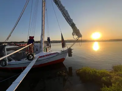 a boat is docked in the water with the sunset at Assuan Felucca in Aswan