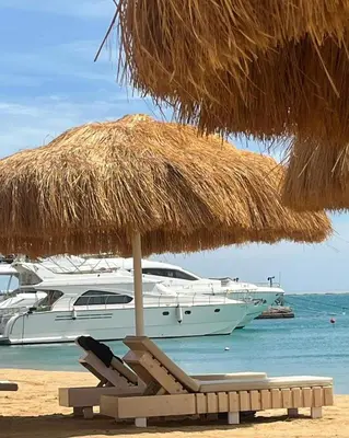 a straw umbrella and chairs on a beach with a boat at Studio Pool & Sea View Princess Resort in Hurghada