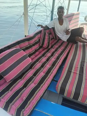 a man sitting on the back of a boat with a bunch of blankets at Felucca Alaska in Aswan