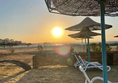 a beach with two chairs and an umbrella and the sunset at Fiesta Beach Resort in Hurghada