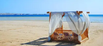 a wooden bed on a beach with white curtains at Luxurious Cozy studio in Sahl Hasheesh Hurghada in Hurghada