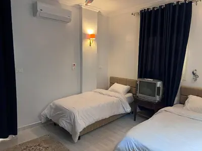 a room with two beds and a tv in it at Spacious Luxury Nile-View Apartment on Upper Floor with Rooftop, Jacuzzi & BBQ ,Steps from Hilton Hotel in Luxor