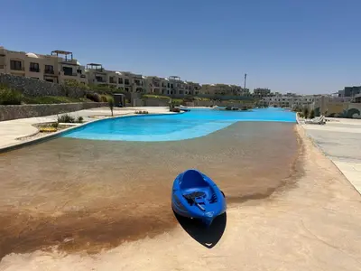 a blue boat sitting on the sand near a swimming pool at One B2b Apartment w balcony with Jacuzzi at Makadi Heights in Hurghada