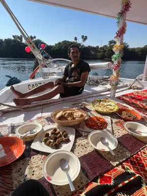 a man sitting on a boat with a table of food at Aswan felucca sailing boat in Aswān