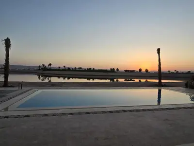 a pool of water with palm trees and a sunset at Villa at Cyan Ring with infinity pool at lagoon in Hurghada