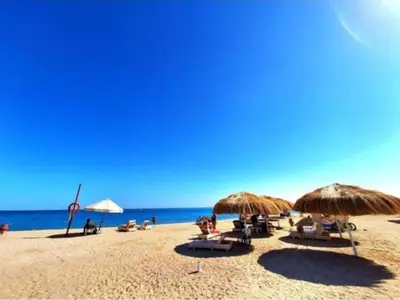 a beach with chairs and umbrellas and the ocean at Niebieski Apartament in Hurghada