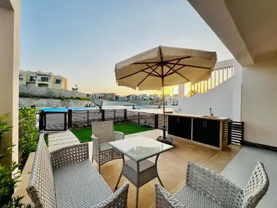 a patio with a table and chairs and an umbrella at Makadi Heights Luxury 1-BR App with Garden & Lagoon View in Hurghada