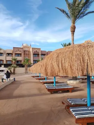 a row of chaise lounges and a straw umbrella on a beach at Tiba Golden in Hurghada