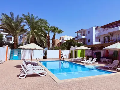 a swimming pool with chairs and umbrellas next to a building at El Fayrouz Guesthouse Luxor in Luxor
