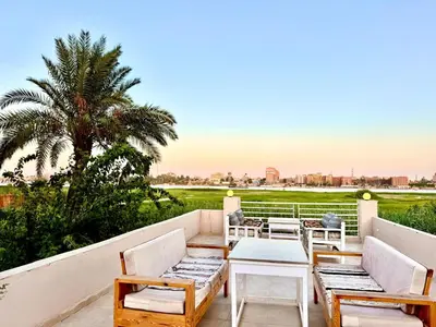 a patio with chairs and a table and a palm tree at Royal Nile Villa - Luxury Nile Sky Penthouse 1 in Al Aqālitah