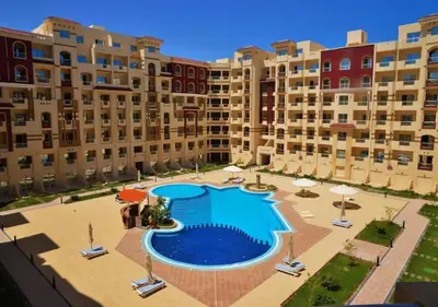 a large pool with chairs and umbrellas in front of buildings at Home 2 Bedroom in Hurghada in Hurghada