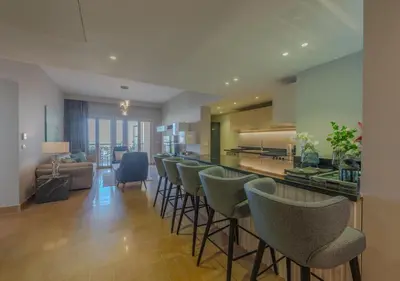 a kitchen with a bar with chairs and a living room at Upscale 2BR Mosaique Marina Stay, Yachts & Sea Views in Hurghada