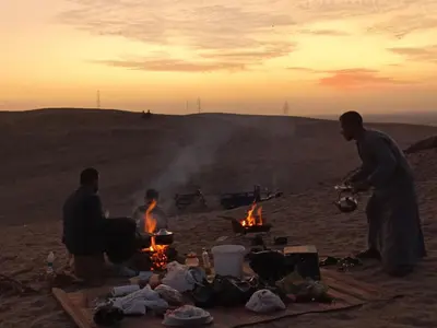 a group of men sitting around a campfire in the desert at Luxor Adventure Guest House in Al Aqālitah