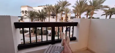 a person standing on a balcony looking out at palm trees at El Gouna Luxury 1BR Golf Apartment at Ancient Sands Resort Pool, Beach & Marina Access in Hurghada