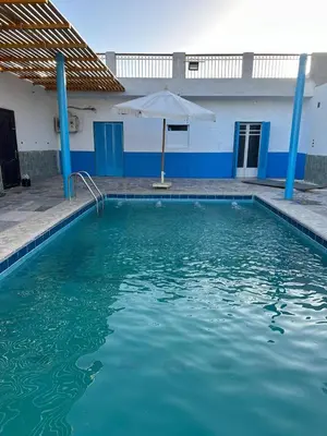 a swimming pool with an umbrella and a blue and white building at Ashria gest house in Jazīrat Salūjah