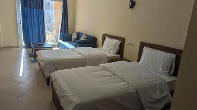 a hotel room with two beds and a blue chair at Studio Apartment Flourenza Hurghada in Hurghada