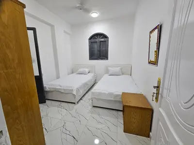 two beds in a room with white walls and marble floors at Hatshepsut Apartments Luxor in Luxor