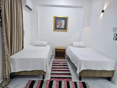 two beds in a white room with a rug at Hatshepsut Apartments Luxor in Luxor