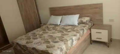 a bed with a wooden headboard and a night stand at جولدن طيبه الذهبيه in Hurghada
