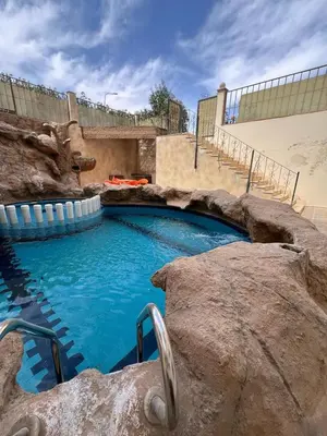 a large swimming pool with blue water and rocks at one bedroom at magawish hurghada in Hurghada