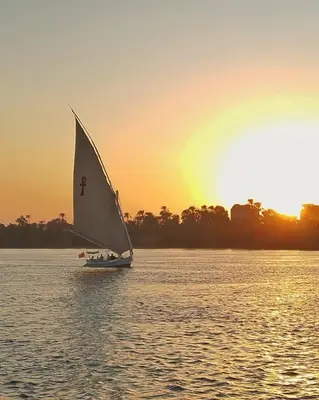 a small sail boat in the water at sunset at Traditional Felucca Sailing Boat Overnight in Aswan