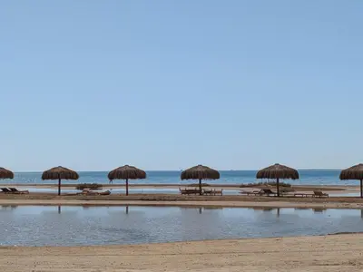 a beach with tables and straw umbrellas and the ocean at Panoramic Seaview Somabay 1BR Apartment in Mesca in Hurghada