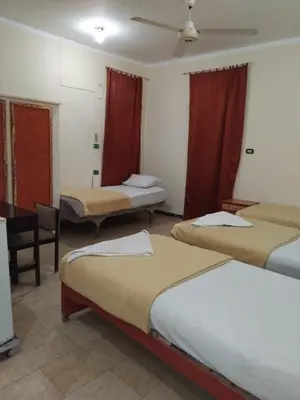 a room with three beds with red curtains at Ramsess Hotel in Luxor