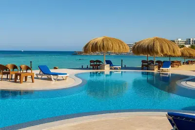 a swimming pool with chairs and umbrellas and the ocean at Aquatic Village - Red Sea Resort in Hurghada