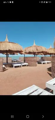 a group of tables and straw umbrellas on a beach at الغردقه قريه فنادير باى in Hurghada