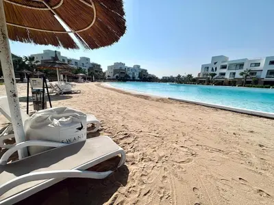 a beach with chairs and an umbrella and the ocean at Comfortable 3BR Apartment in Swan Lake I El Gouna Ground Floor, Garden, Terrace & Lagoon Access in Hurghada