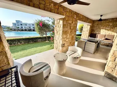 a patio with wicker chairs and tables and a pool at Comfortable 3BR Apartment in Swan Lake I El Gouna Ground Floor, Garden, Terrace & Lagoon Access in Hurghada