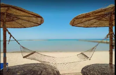 a hammock on a beach with two umbrellas at Amaizing 2BR Apartment B2 in Turtles Beach - Hurghada in Hurghada