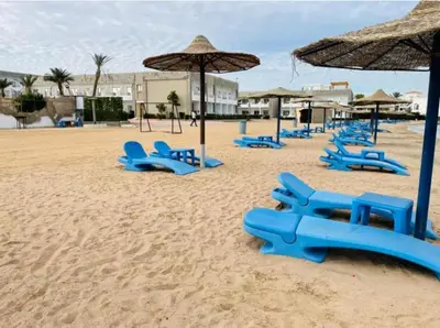 a sandy beach with blue chairs and umbrellas at Cecelia Resort in Hurghada