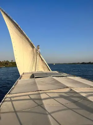 a boat with a white sail on the water at Nile SE Felucca nile cruise private tour in Naj‘ al ‘Amrāb