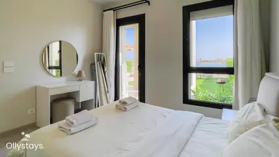 a bedroom with a white bed with a mirror and a window at Ollystays Shedwan 2 BR Pool & lagoon access in Hurghada