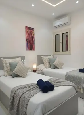two beds in a white room with blue pillows at Hurghada stylish Apartment on the beach in Hurghada
