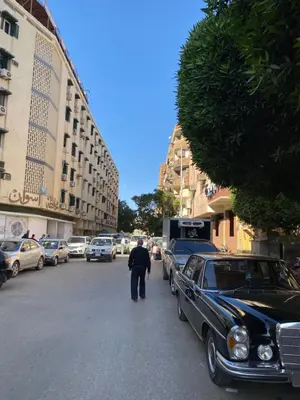 a man walking down a street next to a car at Jme Bunks Hostel in Aswān