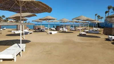 a beach with white chairs and umbrellas and the ocean at Naseem Home in Hurghada