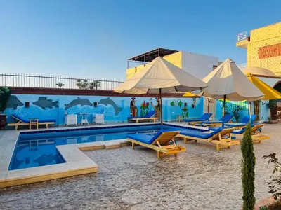 a pool with chairs and umbrellas next to a mural at Horus Golden Luxor in Luxor