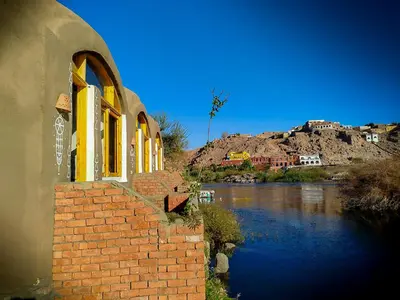 a brick building next to a river next to a mountain at ASSINGAR Island in Aswan