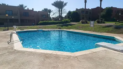a swimming pool with blue water in front of a building at Cozy Chalet In Stella Makadi Beach Resort Hurghada in Hurghada