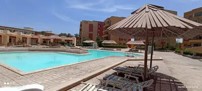 a large swimming pool with chairs and an umbrella at 2-Room Apartment with Swimming Pool in Hurghada
